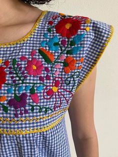 a woman wearing a blue and white checkered dress with flowers on the chestline