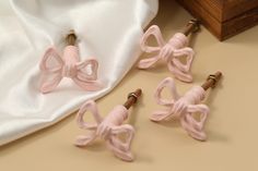 four pink bow tie clips sitting on top of a white cloth next to a wooden box