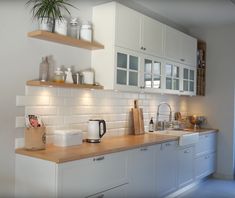 a kitchen with white cabinets and wooden counter tops is pictured in this image, there are plants on the shelves above the sink