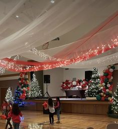 children are playing basketball in an indoor gym decorated with christmas trees and garlands on the ceiling