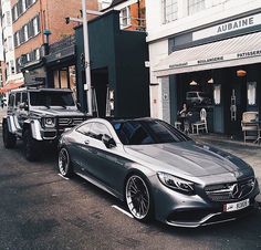 two cars parked on the side of a road next to each other in front of tall buildings