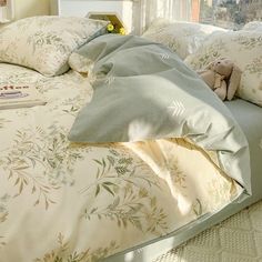 a bed with white sheets, pillows and a teddy bear sitting on top of it