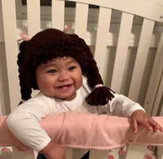 a smiling baby in a crib with a stuffed animal on it's head