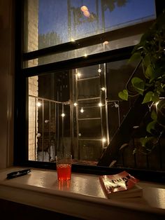 a window sill with a book and drink on it next to a lit staircase