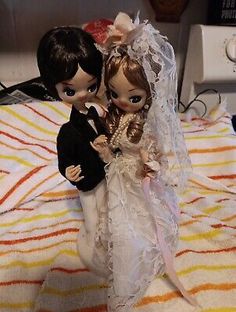 a bride and groom figurine sitting on top of a bed next to each other