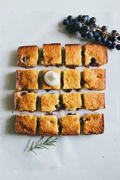 blueberry squares are arranged on a white surface next to berries and a sprig of rosemary