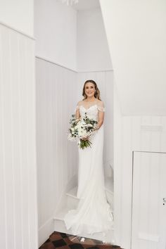 a woman in a wedding dress is standing on the stairs holding a bouquet and looking at the camera