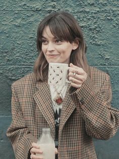 a woman is holding a drink and posing for the camera while wearing a plaid jacket