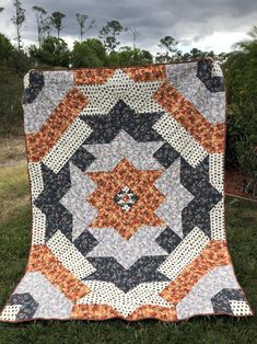 an orange, black and white quilt is on the grass in front of some trees