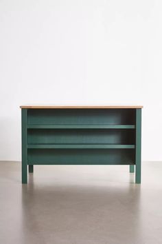 a green shelf sitting on top of a cement floor next to a white wall in an empty room