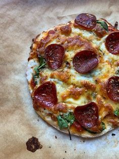 a pepperoni pizza sitting on top of a piece of wax paper covered in green leaves