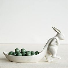 a white ceramic rabbit sitting on top of a bowl filled with green candy balls in front of a white wall