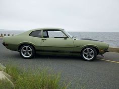 a green car is parked on the side of the road near the water and grass