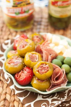 a plate with olives, ham and tomatoes on it next to two jars of pickles