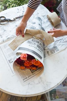 a woman is wrapping flowers on top of a table with scissors and paper towels around it