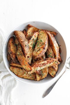 a white bowl filled with fried potatoes on top of a table next to a fork