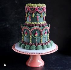 a three tiered cake decorated with pink and green icing on a plate in front of a black background