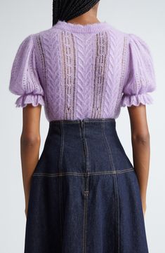 the back of a woman wearing a purple sweater and denim skirt, with her hands in her pockets