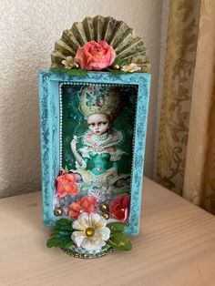 an altered picture frame with flowers and a doll in the center is on a table