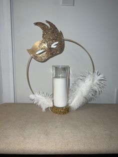 a candle sits on a table next to a masquerade mask and white feathers