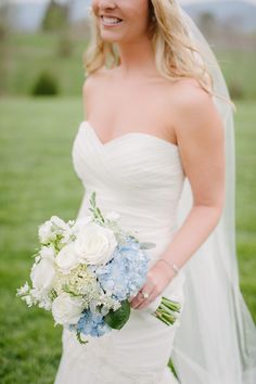 a woman in a wedding dress holding a bouquet of flowers and smiling at the camera