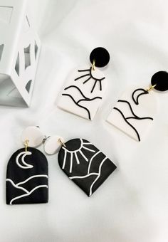 three pairs of black and white earrings sitting on top of a white table next to an object