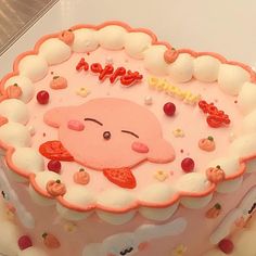 a pink cake with white frosting and fruit decorations on it's face is sitting on a table