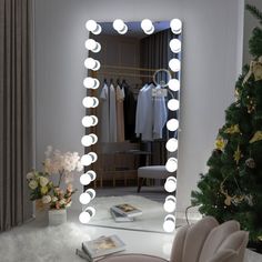 a room with a mirror, chair and christmas tree in front of the window that has lights on it