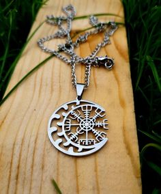 a wooden board with a metal pendant on it's side and grass in the background