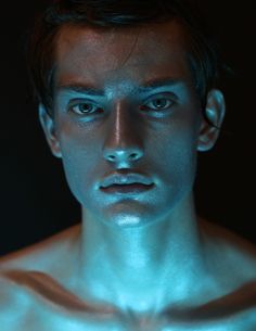 a man with blue paint on his face and chest is looking at the camera while standing in front of a black background