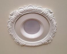 a white ceiling light with an ornate frame around the base and center piece on the wall