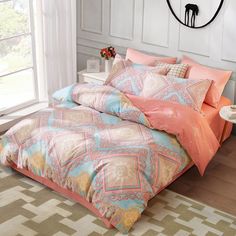 a bed with an orange and blue comforter next to a window