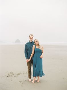 a man and woman standing on the beach in front of an ocean with foggy sky