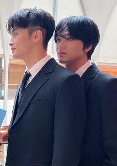 two young men in suits are standing next to each other and looking off into the distance