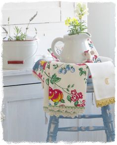 an old stool with flowers on it next to a potted plant and tea towel