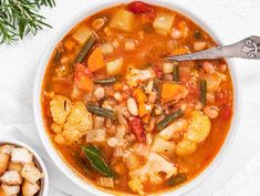 a white bowl filled with vegetable soup next to a spoon