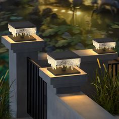 three lights that are sitting on top of some concrete blocks in front of plants and water