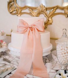 there is a wedding cake with pink ribbon on the table next to other desserts