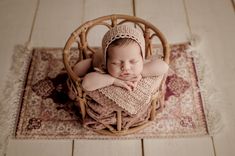 a baby sleeping in a wicker basket on top of a rug wearing a bonnet