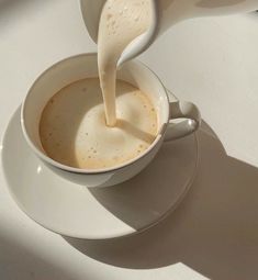 a person pouring milk into a cup on a saucer