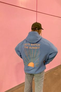 Girl standing in front of pink background wearing a blue Dandy Worldwide hoodie that says "Let's Watch the Sunset" Graphic Hoodie Outfit, Hoodie Casual Outfit, Cloud Clothes, Dandy Worldwide, Sunset Watching, Sunset Hoodie, Watch The Sunset, Embroidery Hoodie, Celestial Art