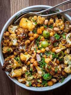 a bowl filled with lots of food on top of a wooden table next to a fork