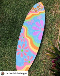 a colorful surfboard laying in the grass with flowers painted on it's side