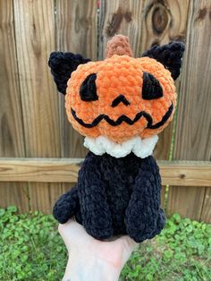 a hand holding a small stuffed animal with a pumpkin on it's face and eyes