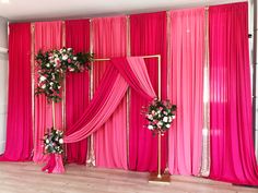 a pink backdrop with flowers and greenery in front of it, set up for a wedding ceremony