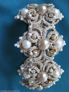 a brooch with pearls on it sitting on a blue cloth covered surface, in the shape of an intricate design