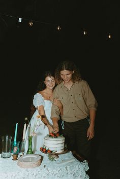 a man and woman cutting into a cake on top of a white cloth covered table