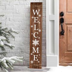 a welcome sign hanging from the side of a brick wall next to a christmas tree