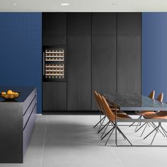 a modern kitchen with blue walls and white flooring, black countertops and wooden chairs