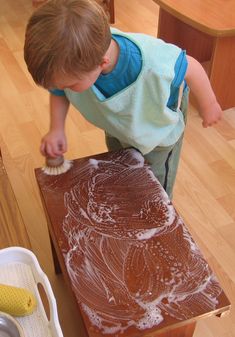 a young boy standing on top of a wooden table next to a bowl and brush